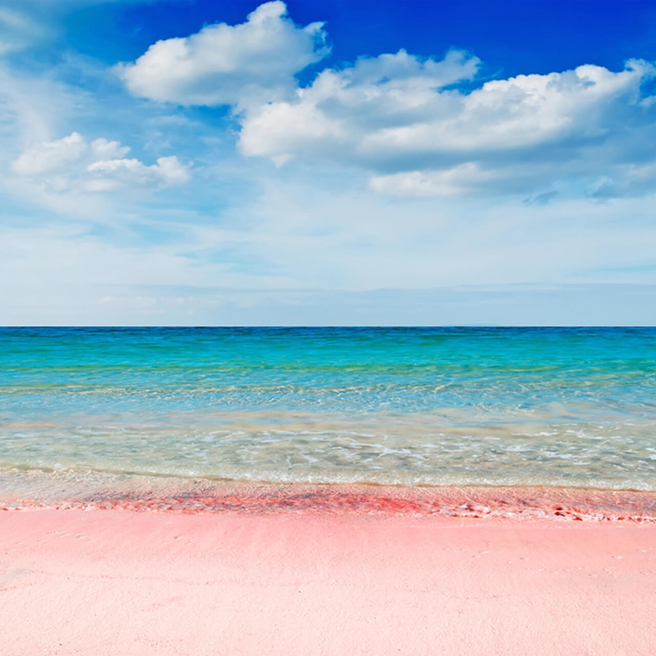 Scenic view of the Spiaggia Rosa, famous for its unique pink sands, with clear turquoise waters of the Mediterranean Sea under a bright blue sky dotted with fluffy white clouds.