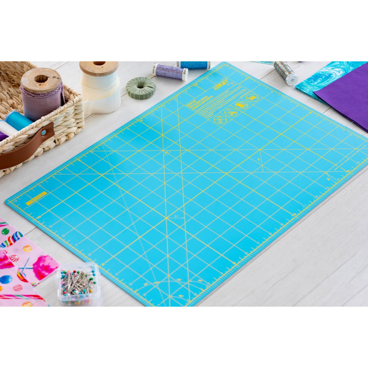 OLFA Aqua Cutting Mat laid out on a crafting table with sewing supplies including thread spools, fabric, and pins, showcasing a practical and vibrant sewing setup.