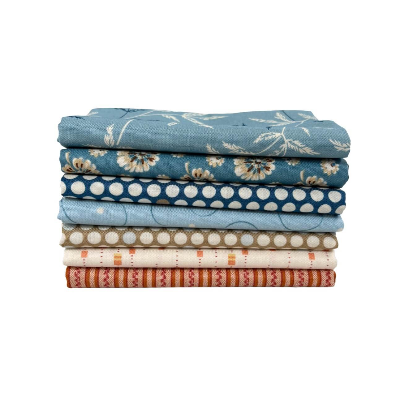 Blue Sunday Fat Quarter Bundle by Laundry Basket Quilts, featuring seven blue, orange and cream floral and tonal prints stacked neatly.