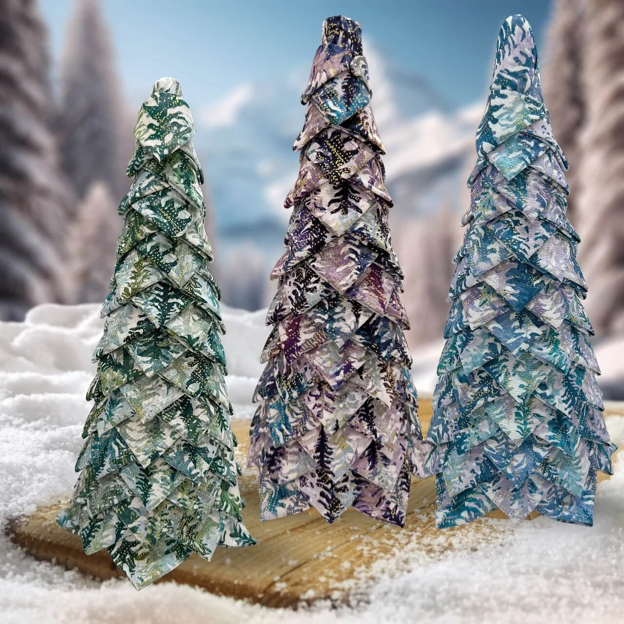 Group of three no-sew fabric trees in prints from the Hill Shine collection, displayed outdoors in a snowy winter setting.