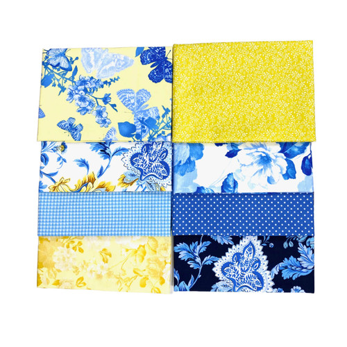 A collection of six square fabric pieces, neatly arranged in two rows, showcasing a variety of patterns. The top row features butterfly and floral prints in shades of blue on a yellow background, and a yellow fabric with a small, intricate white floral pattern. The bottom row includes a blue and yellow floral design, a blue gingham pattern, polka dots on a navy background, and a dark blue fabric with a large, ornate white floral motif. The collection presents a harmonious blend of blues and yellows, suggesting a selection of high-quality cotton quilting materials.
