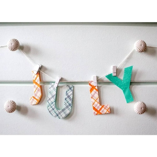 Decorative banner spelling "JOY" with letters cut from fabric and bonded using HeatnBond Ultrahold, hung on a string with clothespins against a light wall.