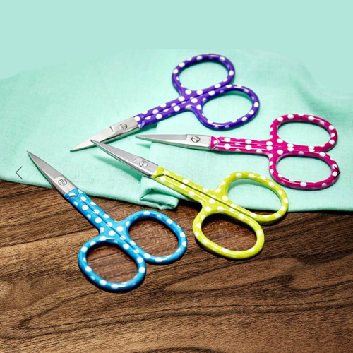 Sew Tasty polka dot  embroidery scissors in pink, purple, green and teal on light green fabric on a dark tabletop.