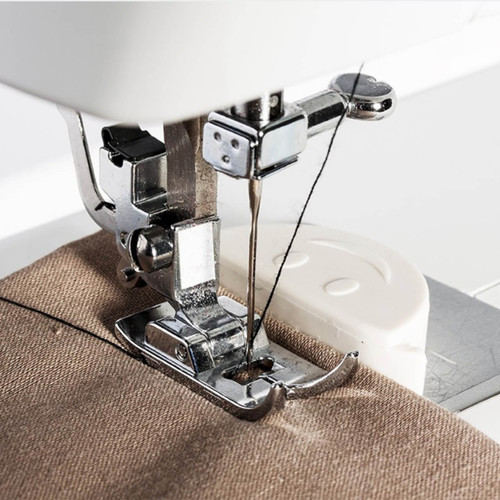 Close-up of white magnetic seam guide on the throat plate, keeping fabric aligned beside the presser foot for a straight seam.