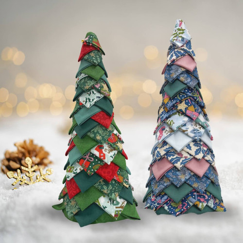 Two handmade no-sew Christmas trees made with Liberty fabrics, one in classic green and red prints and the other in blue, pink, and cream fabrics, shown on a snowy festive background.