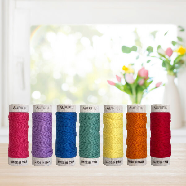 An image of 7 Aurifil 8WT spoons on a tabletop in front of a window with vases of flowers