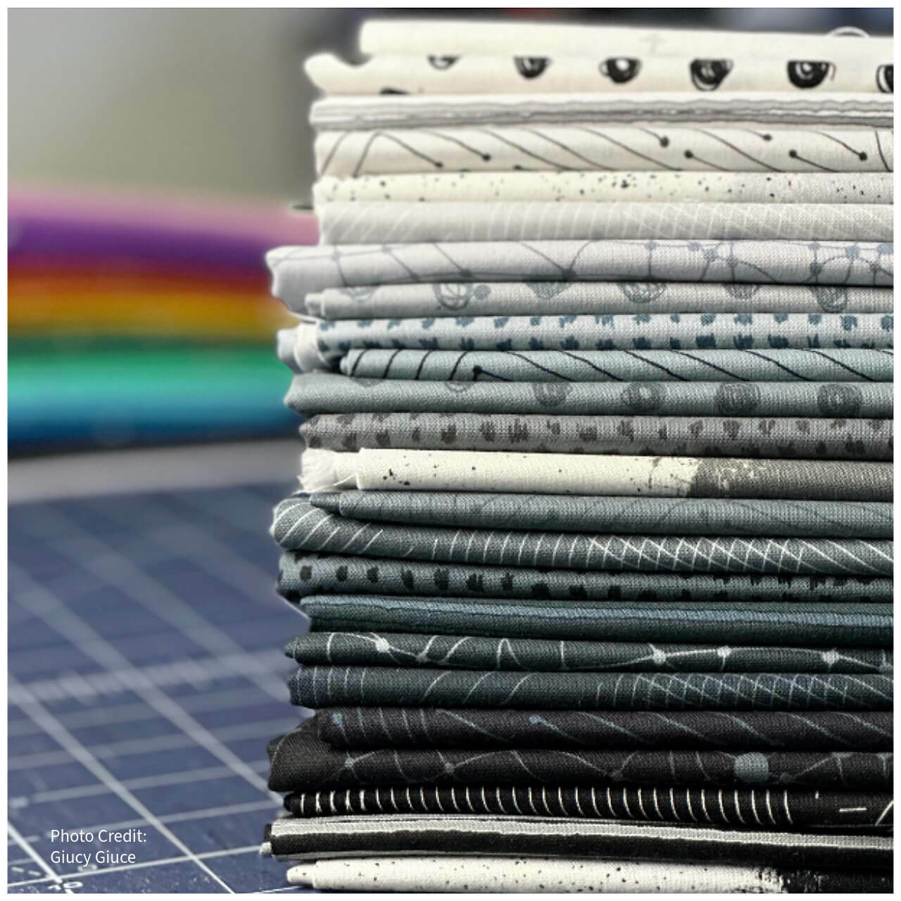 Stack of various monochromatic fabrics from the Ink Collection by Giucy Giuce, featuring geometric designs, doodles, and two-tone patterns in black, grey, and white.