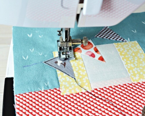 Sewing machine zigzag-stitching appliqué bunting onto a colourful patchwork quilt block.