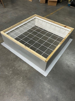 Wood-framed roof curb with white safety grid mesh sitting on a warehouse floor