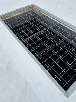 Overhead view of a flush-mounted wire safety screen set into a white commercial roof opening