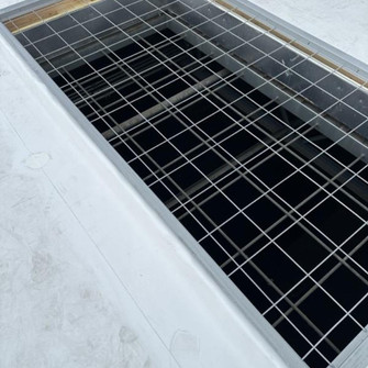 Overhead view of a flush-mounted wire safety screen set into a white commercial roof opening