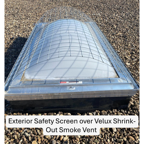 Wire exterior safety screen fitted over a Velux shrink-out smoke vent on a gravel roof, close-up