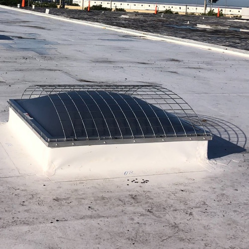 Domed skylight with a protective wire guard installed on a white commercial roof under blue sky