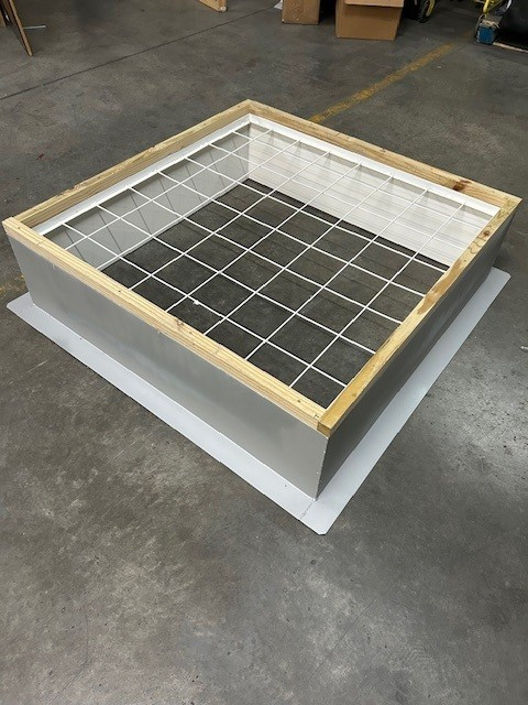 Assembled roof curb with a wire safety grate on top, photographed indoors on a warehouse floor