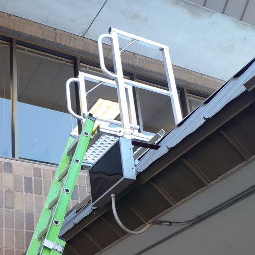 Green extension ladder resting against a white KD001 ladder dock landing platform mounted at a commercial roof edge