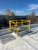 Yellow safety railing with self-closing gate installed around a roof hatch, office building visible behind