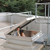 Person climbing through an open roof hatch with a safety railing on a gravel rooftop