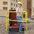 Woman in a hard hat climbing through an open roof hatch with yellow safety railing, city skyline behind