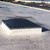 Domed skylight with a protective wire guard installed on a white commercial roof under blue sky