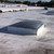 Domed Velux CMD2 skylight with a wire safety grille installed on a white membrane roof under clear blue sky