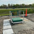 Green-painted guardrail installed around a green roof hatch on a gravel ballast roof, road nearby
