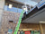 Green extension ladder resting against a white KD001 ladder dock landing platform mounted at a commercial roof edge