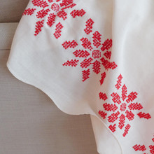 Vintage white linen tablecloth with red hand embroidered flowers.  The red floral design stands out against the white background of the tablecloth.  Close up of the cross stitch design.