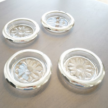 Set of three vintage silverplate and glass coasters laid out on a coffee table with the sun reflecting in the shine of the silver