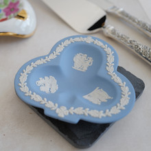 The dish has scalloped raised edges and features a classical design in white against the light blue background.  There is a relief of figures.