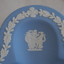 This is a close up of a vintage ring dish is in a club shape and features a classical design in white against the light blue background.