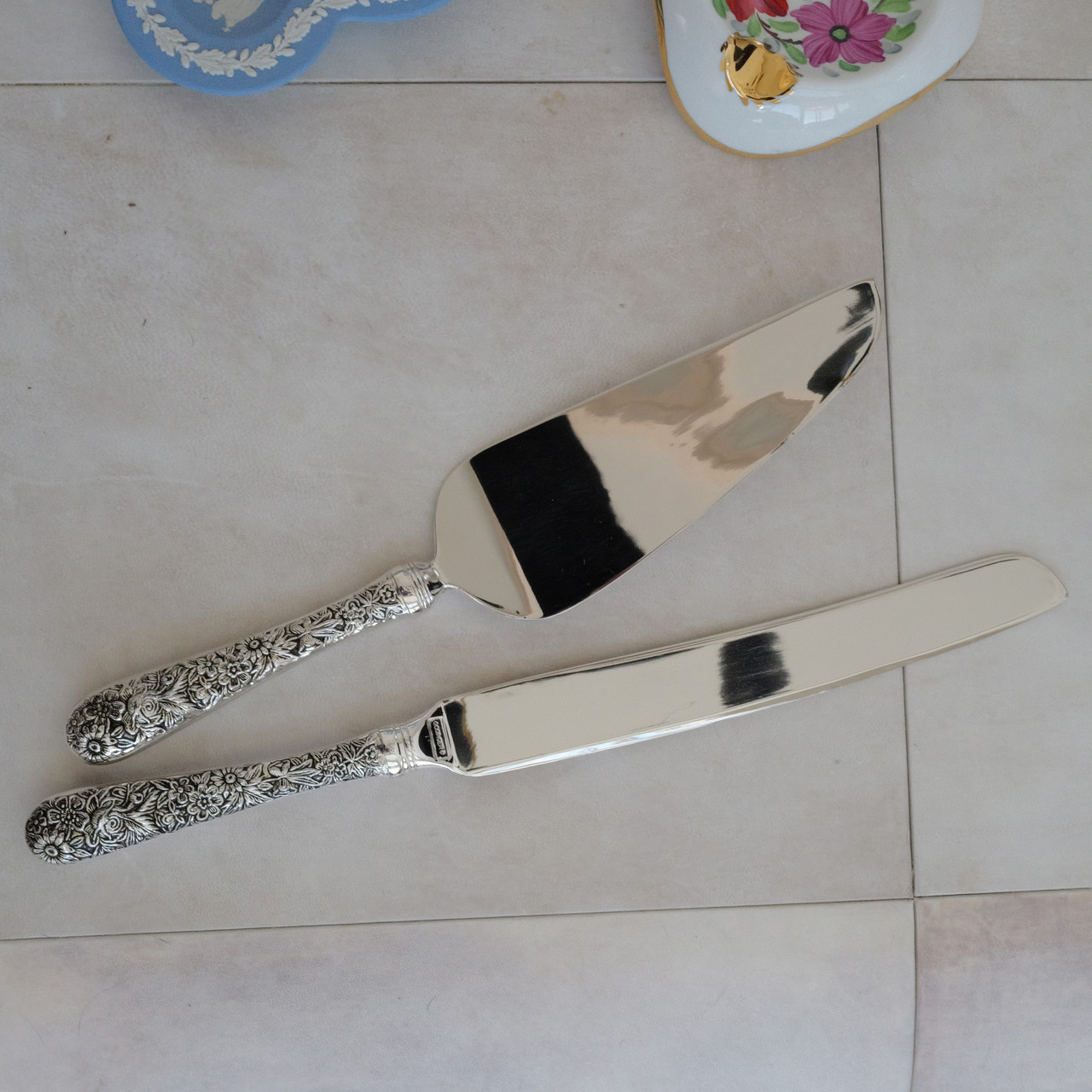 Vintage cake serving set with ornate embossed floral handles.  The set includes a cake knife and a cake server .  Both serving utensils are made with stainless steel blades and ornate silver plated handles.  These elegant pieces have a high gloss shine.