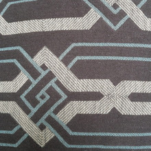 The charcoal grey background of the pillow case is rich and saturated and trends towards brown with light blue and white chained geometric woven diamonds as the pattern.