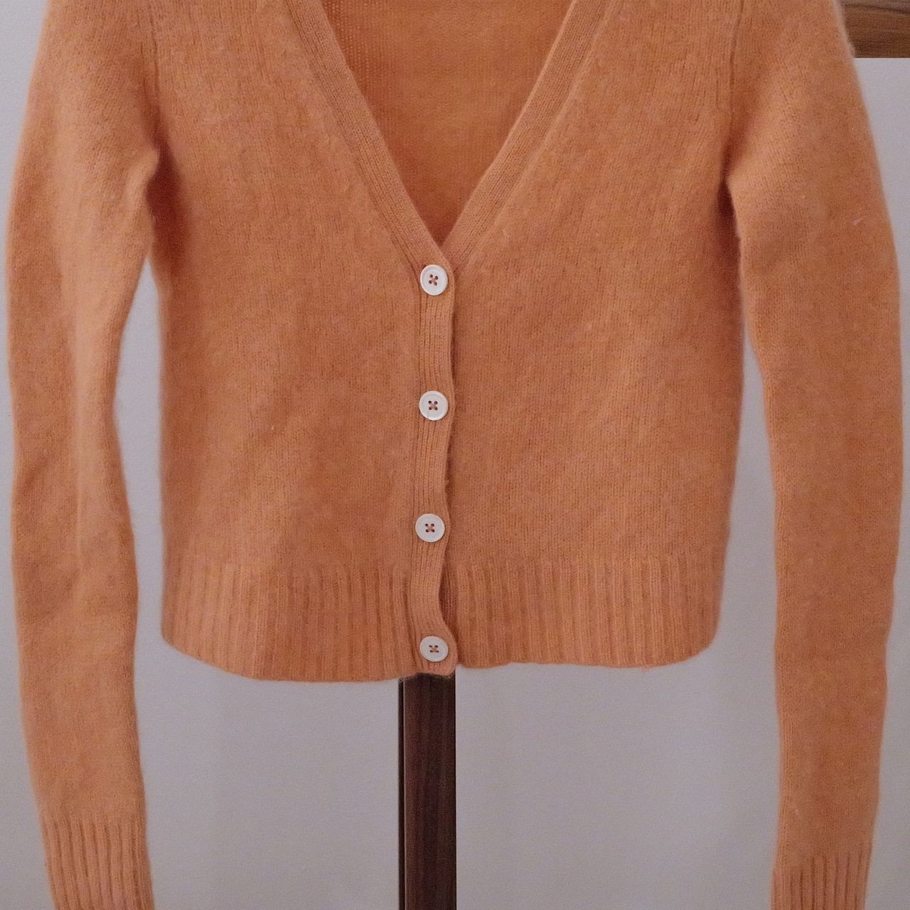 A soft and cozy 100% cashmere cardigan in peach-orange, perfect for layering in every season.