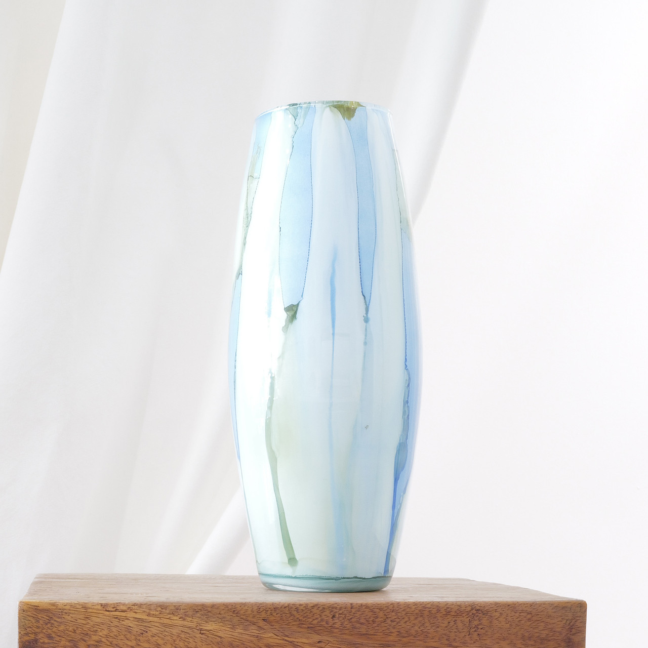 This tall glass vase features flowing vertical washes of blue and green that resemble watercolor brushstrokes. Its surface has a soft, translucent quality that catches light beautifully.