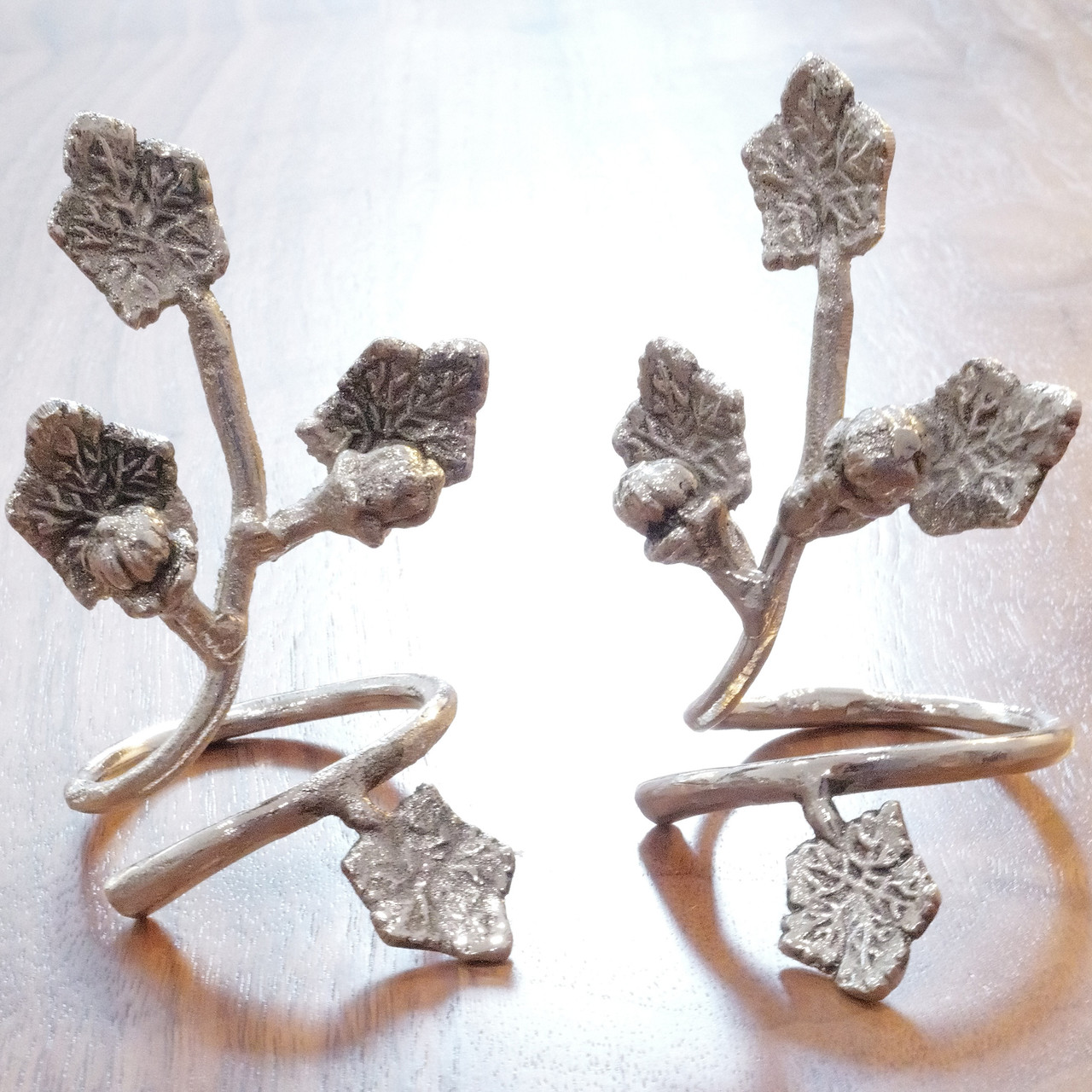 Set of two vintage cast metal napkin rings featuring leaf and berry design, rustic silver finish, perfect for elegant dining table decor or gifts.