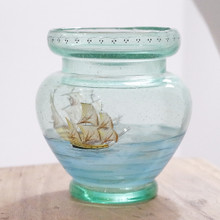 Blue glass vase with a scene of painted ships on sailing water.