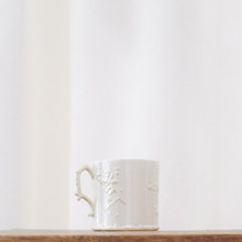 This vintage Belleek porcelain mug has a distinct design with a cream color, glossy shine, is decorated with raised yellow flowers on a stem, and the handle is a twig.