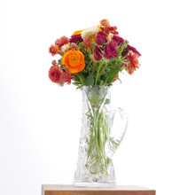 Fresh flower bouquet of a mix of ranunculus, strawflower, spray roses, and astilbe in the full spectrum of sunset colors.