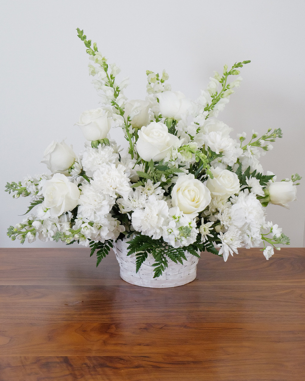 Peace and Condolences Lush white funeral basket arrangement with roses, snapdragons, carnations, chrysanthemums, and greenery.