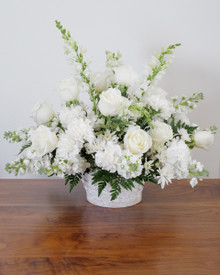 Lush white funeral basket arrangement with roses, snapdragons, carnations, chrysanthemums, and greenery.