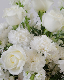 Classic white roses and textured seasonal flowers create a peaceful memorial arrangement.