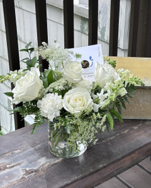 Elegant white floral arrangement featuring roses, snapdragons, carnations, and delicate seasonal blooms.
