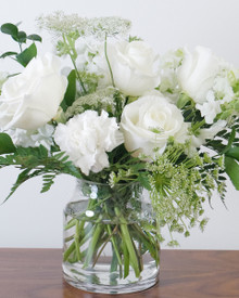 Airy white funeral arrangement featuring premium white blooms and fresh green foliage.