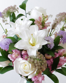 Garden-inspired baby girl arrangement with white lilies, roses, pastel blooms, and fresh greenery.