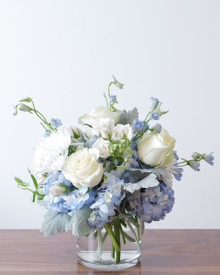 Detail of white mums, cream spray roses, and light blue delphinium against blue hydrangea