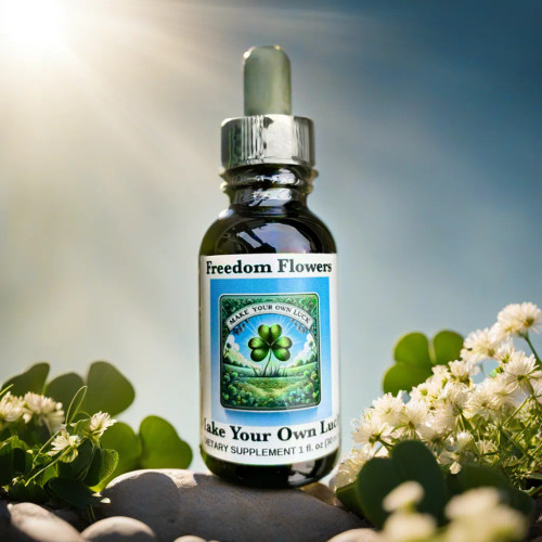 Bottle of Make Your Own Luck essence sitting on a rock surrounded by clover and flowers with sunlight streaming in the background.