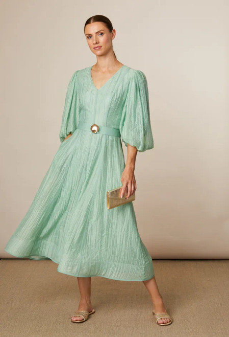 Fee G Apple Green A-line dress with sleeves (883B/124). The Kylie Dress is a beautifully fluid midi dress in a fresh green hue. Constructed in a textured tencel fabric with a flattering V-neckline, side pockets and weighted hem. Statement puff sleeves add a romantic touch, while the belted waist with gold-tone seashell buckle detail enhances the silhouette.