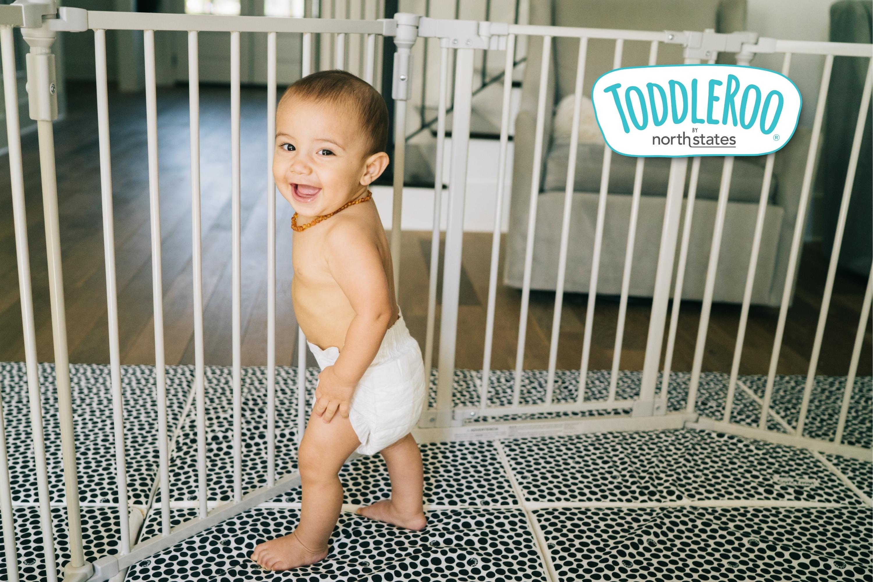 Baby smiling while standing inside a taupe metal superyard