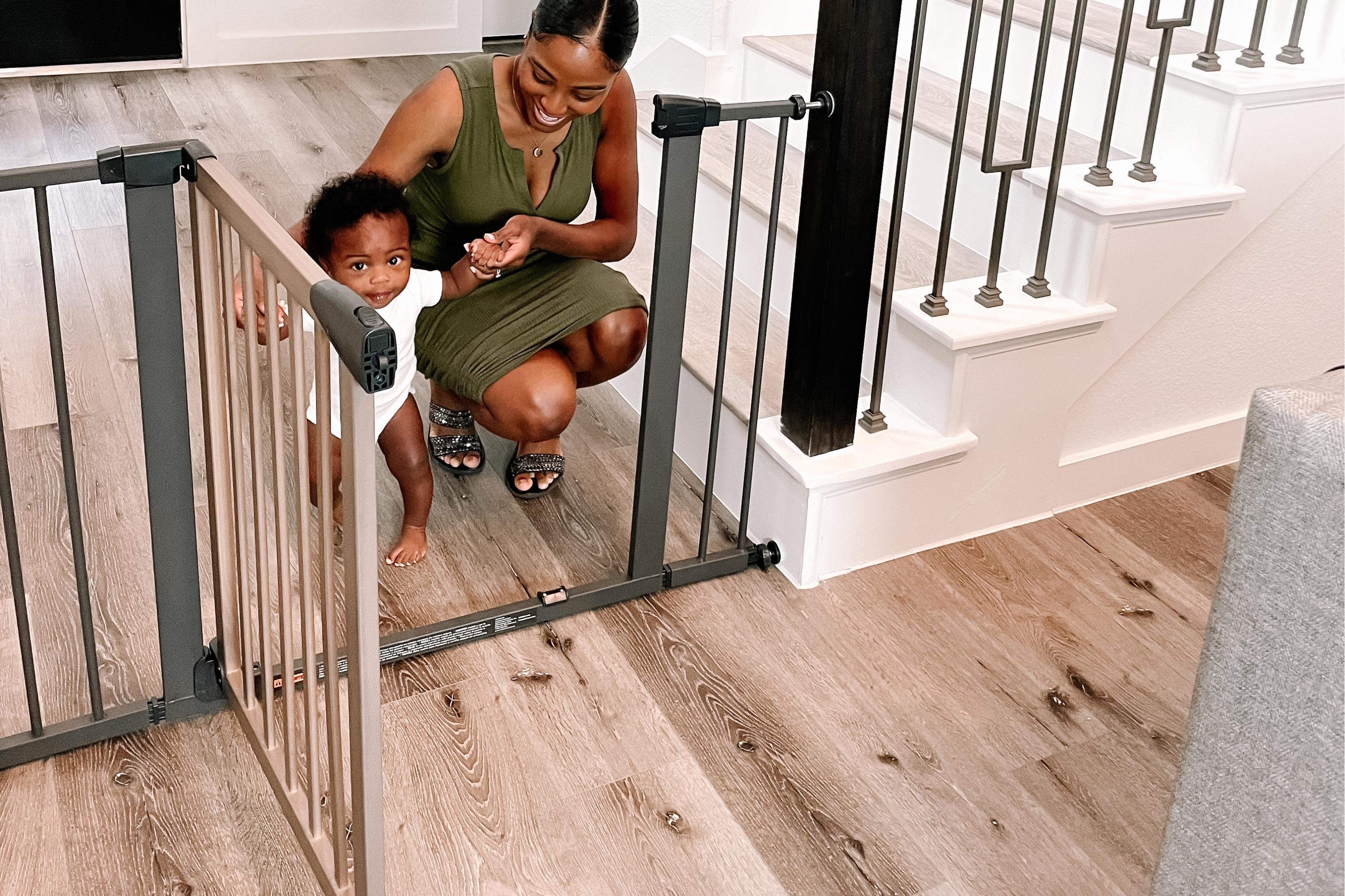 Mom smiling while helping her baby walk through a Driftwood Extra Wide Auto Close Gate