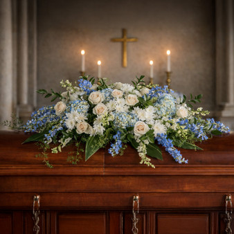 Timeless Essence casket spray featuring roses, hydrangea, delphinium, and snapdragons arranged for a funeral service